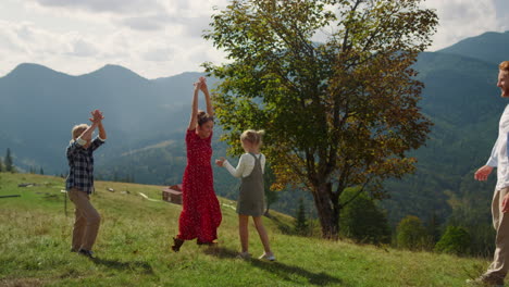 family playing active game on mountains. parents running with kids on grass.
