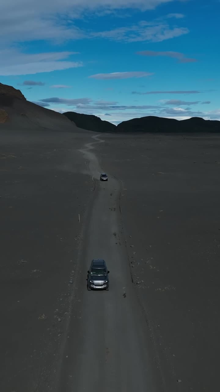 Filmato aereo di droni di auto che guidano su una strada di sabbia nera. Inquadratura verticale