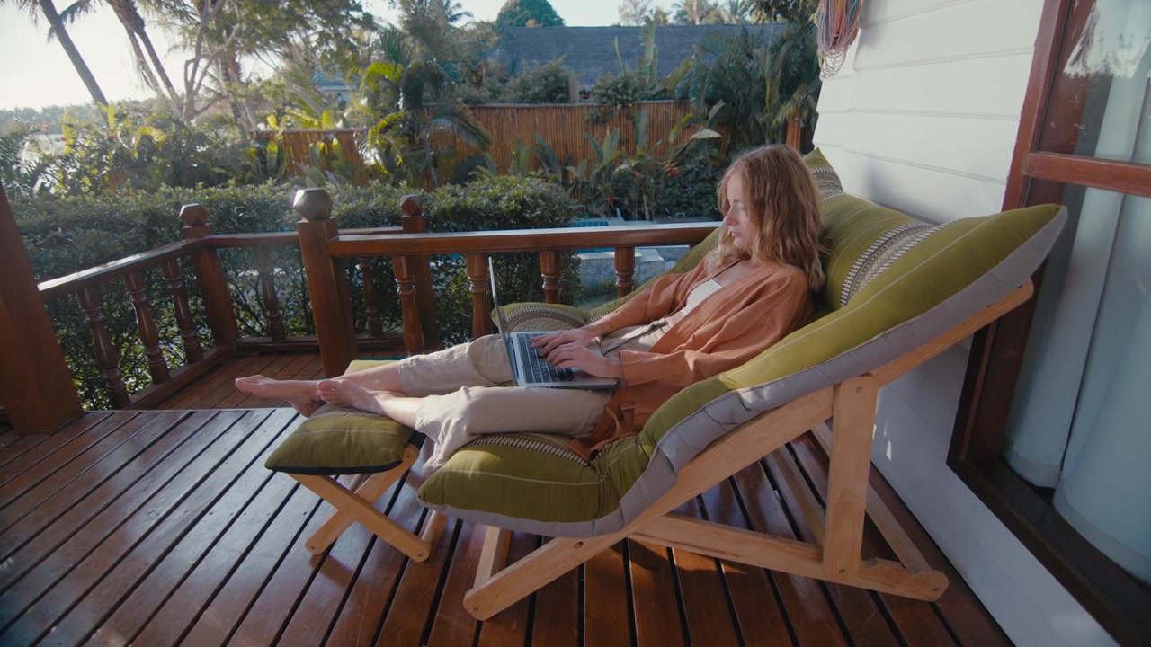 Giovane donna che lavora al laptop su un balcone tropicale.