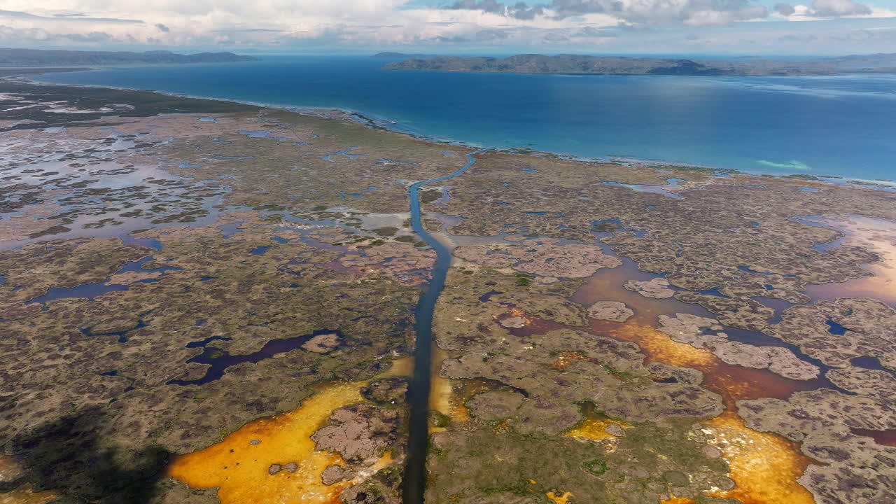 Aerial drone view of a waterway channel cutting through the totora reeds of the Uros floating islands on Lake Titicaca near Puno, Peru. The vast lake and Andes mountains stretch into the distance