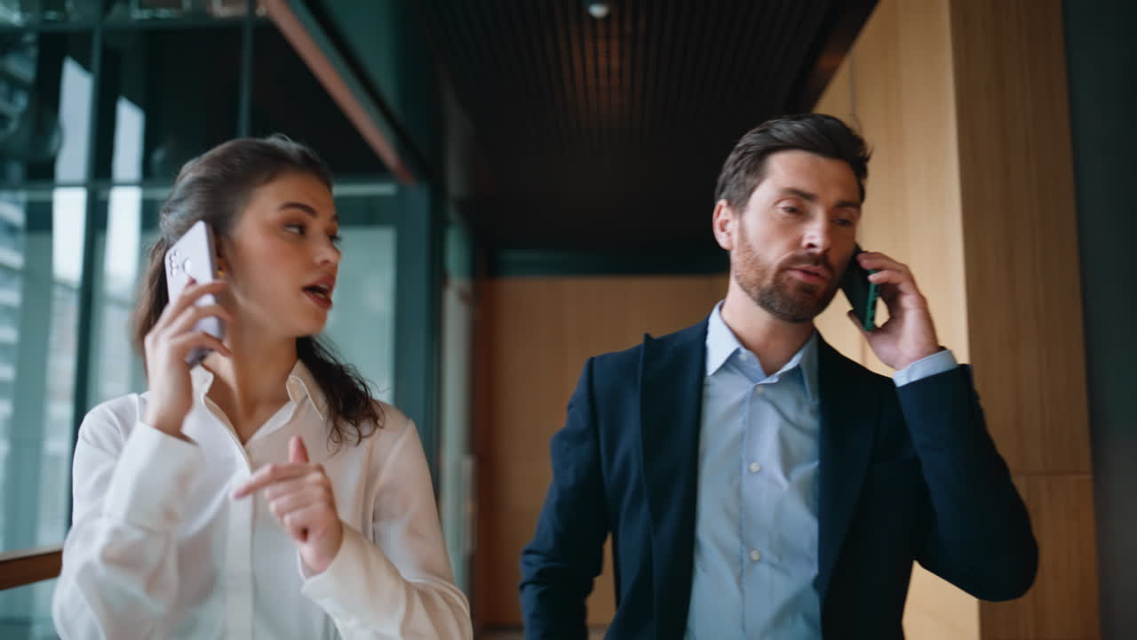 Office colleagues talking cellphones walking hallway closeup. Friendly woman man