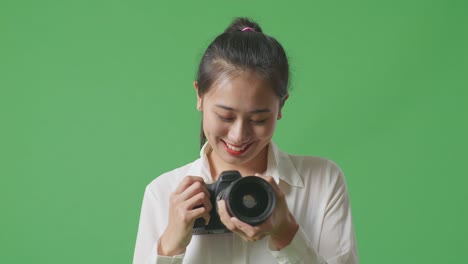 close up of asian photographer changing lens of camera before using it taking pictures while standing on green screen background in the studio