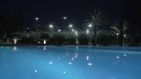 Una-Toma-De-Steadicam-De-La-Superficie-Brillante-De-Una-Piscina-Abierta-Con-Iluminación-Nocturna