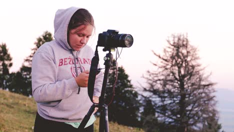 a young caucasian girl preparing her camera for timelapse shooting, capturing stunning footage of alpine meadows in the summer