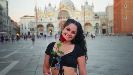 Chica-Con-Rosa-Roja,-Camisa-Negra,-Sonriente,-En-La-Ciudad,-Torre-Al-Fondo,-Venecia,-Italia