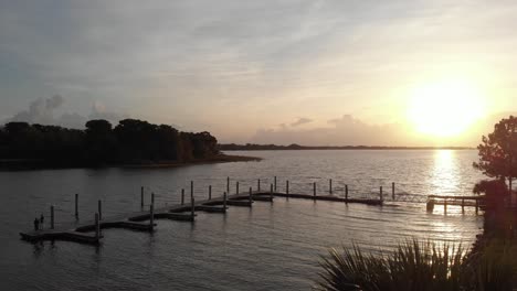 Sonnenstrahlender-Vogel,-Der-An-Einer-Drohne-Vorbeifliegt,-Weitwinkelaufnahme-Des-Yachthafens-Mit-Leuchtturm-An-Den-Palmen-Der-Bucht