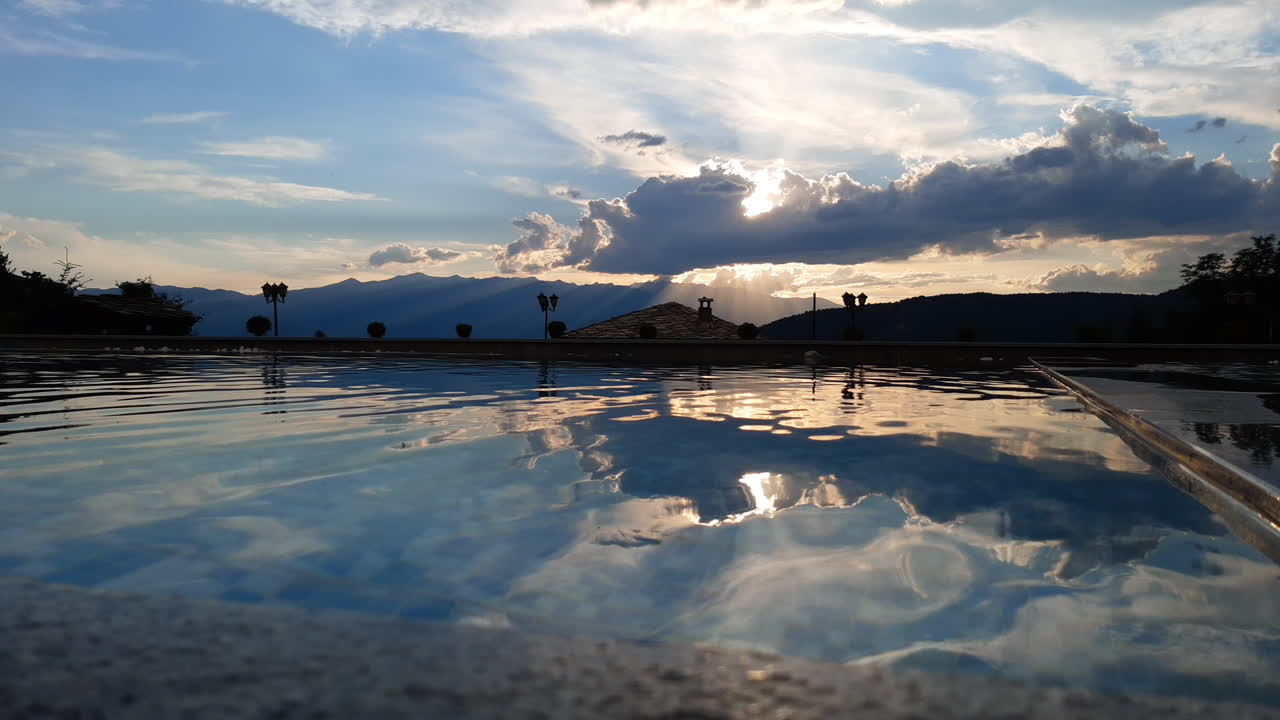 Infinity pool with beautiful mountain view at sunset. Sun rays shine behind the clouds.