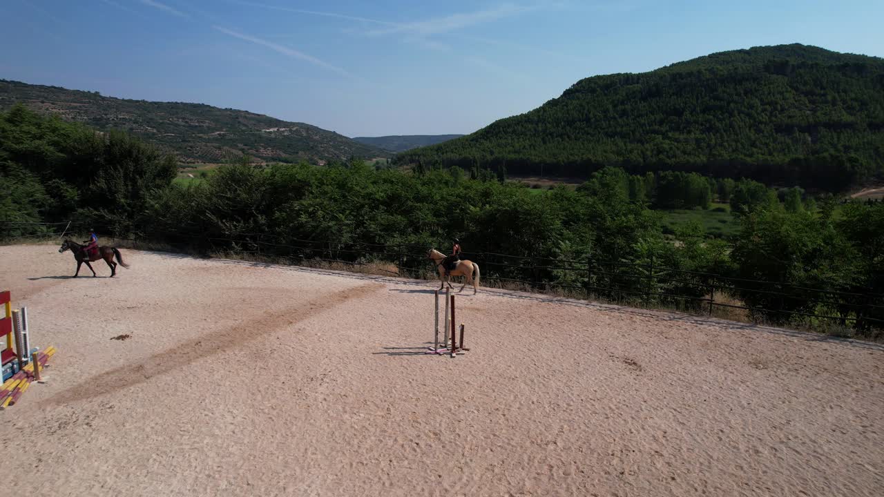 Slow motion aerial dolly in frames two riders training on a track surrounded by green mountains on a sunny day