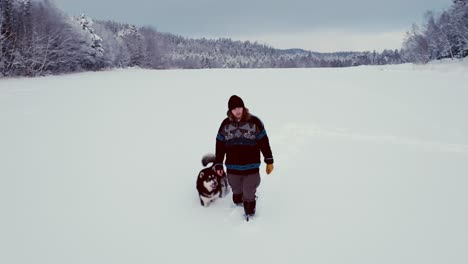 a man in winter clothes is walking in deep snow with his alaskan malamute dog