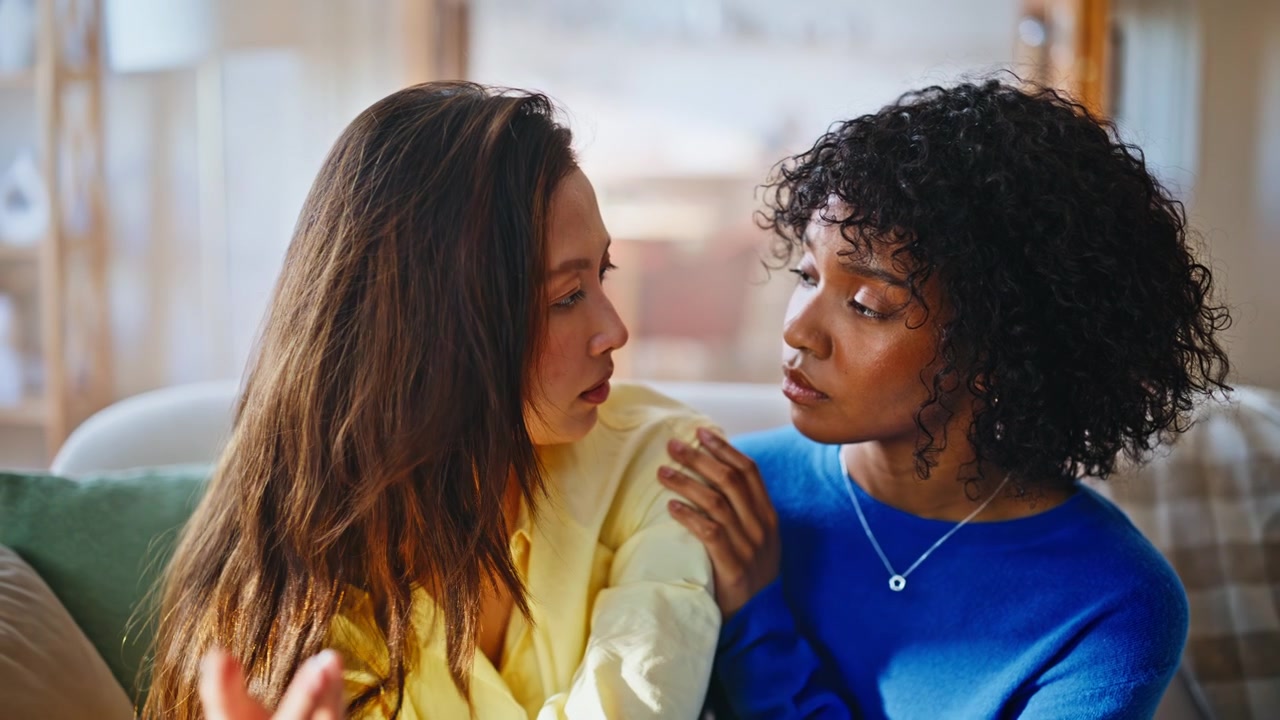 Upset woman consoled by caring friend home sofa. Emotional talk between friends.