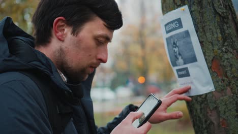 a man reads an advertisement about the loss of a dog in a tree in the park and calls the owner at the phone number indicated in the poster. the theme of the missing search for missing pets. lost dog