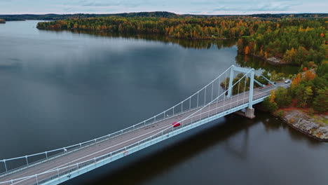 slowmotion high angle shot of a suspension bridge crossing a huge lake surrounded by an autumn forest with red, green yellow and brown trees