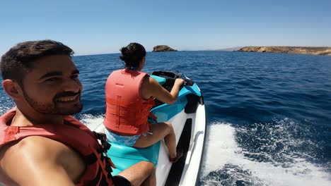 a couple rides a jet ski on the open ocean under a clear blue sky, enjoying a summer adventure near a coastline.
