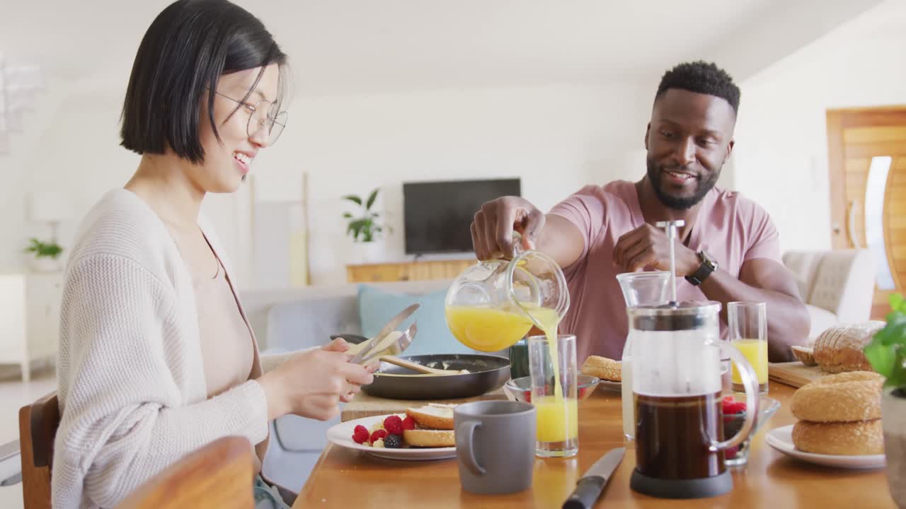 pareja feliz y diversa sentada a la mesa y desayunando