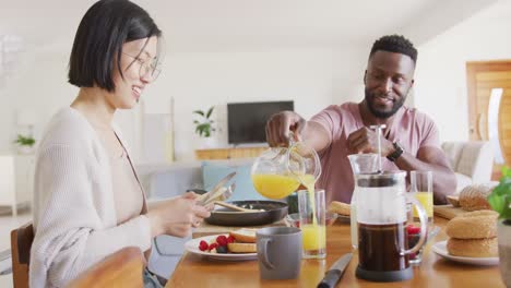 Happy-diverse-couple-sitting-at-table-and-having-breakfast