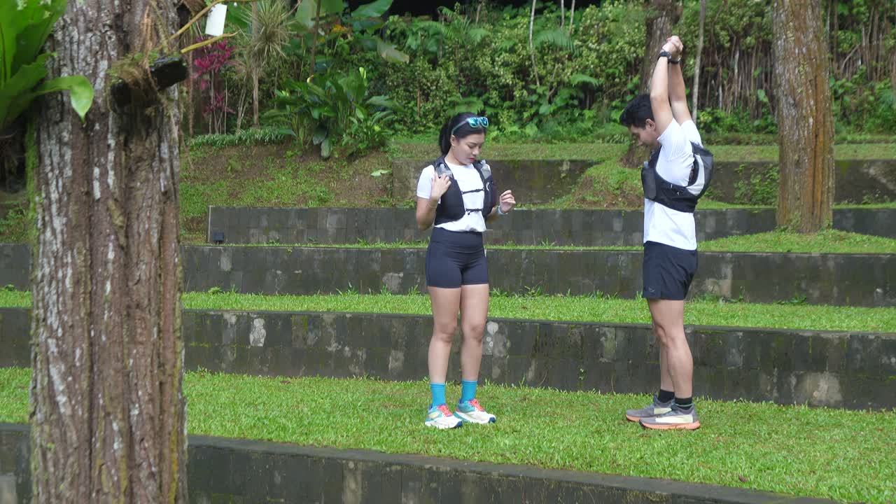 An Asian couple puts drink pouches into their vest pockets before starting their workout in a tree-filled park