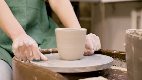 close up view of hands of a clerk cutting a piece of pottery with a thread on a potter wheel in a workshop