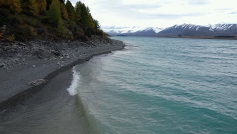 waves in the coastline of lake tekapo with snowy mountains in the background in south island, new zealand. - aerial shot