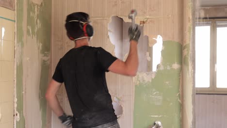 contratista masculino perforando un agujero en la pared con un pequeño martillo durante la renovación