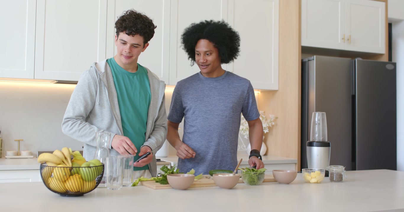 African American men in kitchen cutting greens on boards reaching for apple passing and making meal