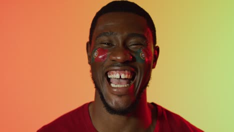retrato de un feliz partidario afroamericano con la bandera de portugal en las mejillas sobre la iluminación rosa