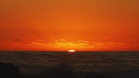 golden sun setting below horizon over rough ocean waves - static shot