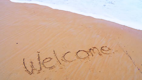 envíe un mensaje de texto de bienvenida en la playa del mar y salpicando olas en la arena con la ola de cámara lenta en el concepto de naturaleza