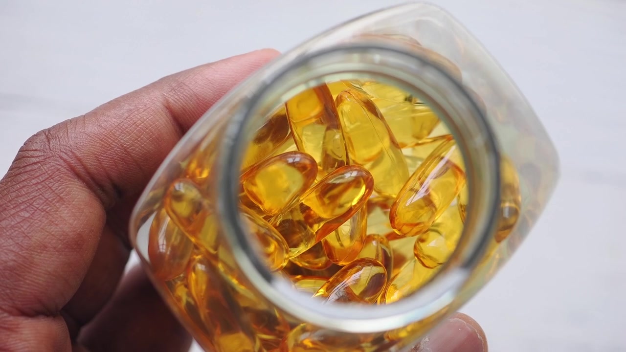 Mano che tiene un barattolo di vetro riempito con capsule dorate di olio di pesce Omega-3