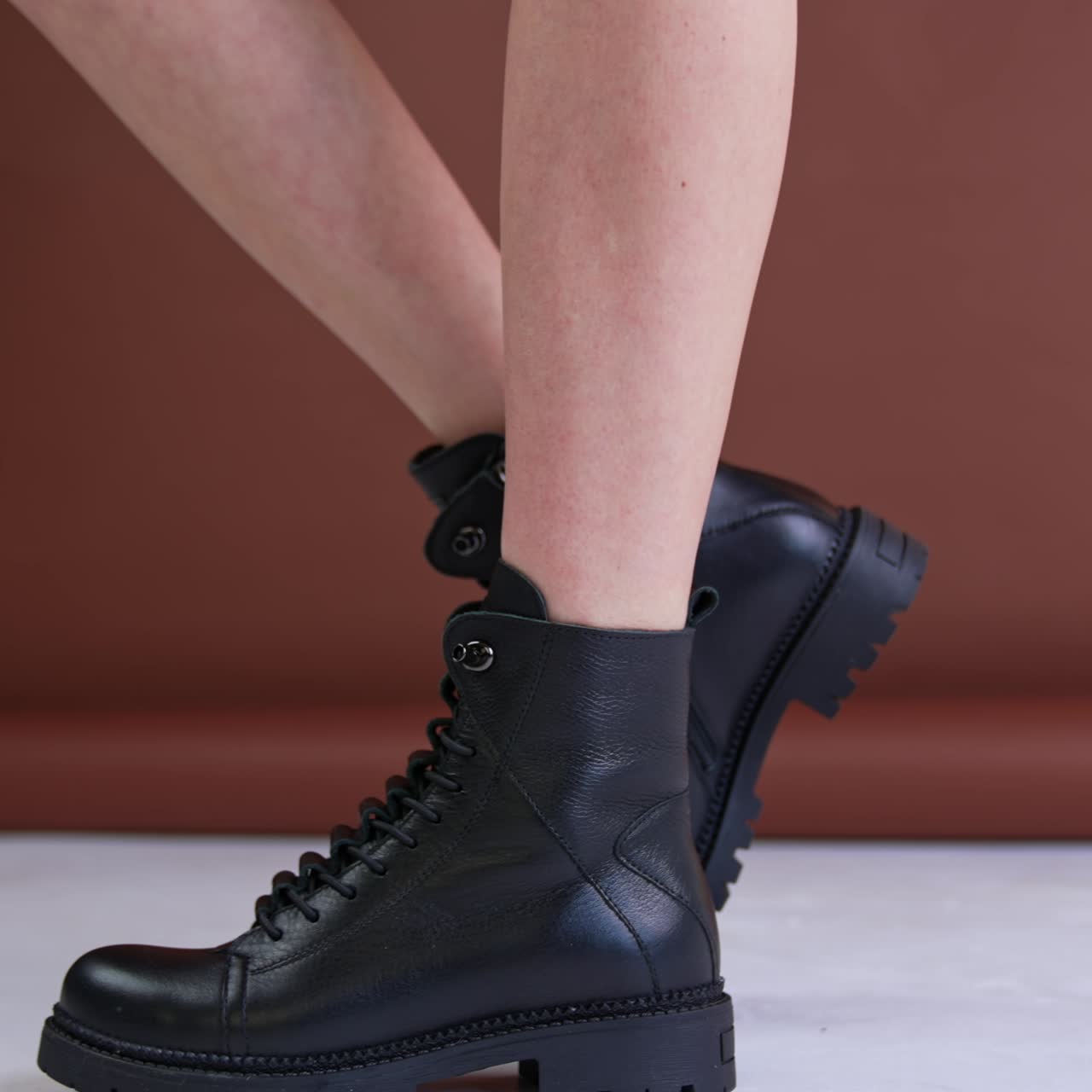 Low black leather boots on a bare-legged woman. Model turns to show her fashionable shoes on plain soles. Brown backdrop