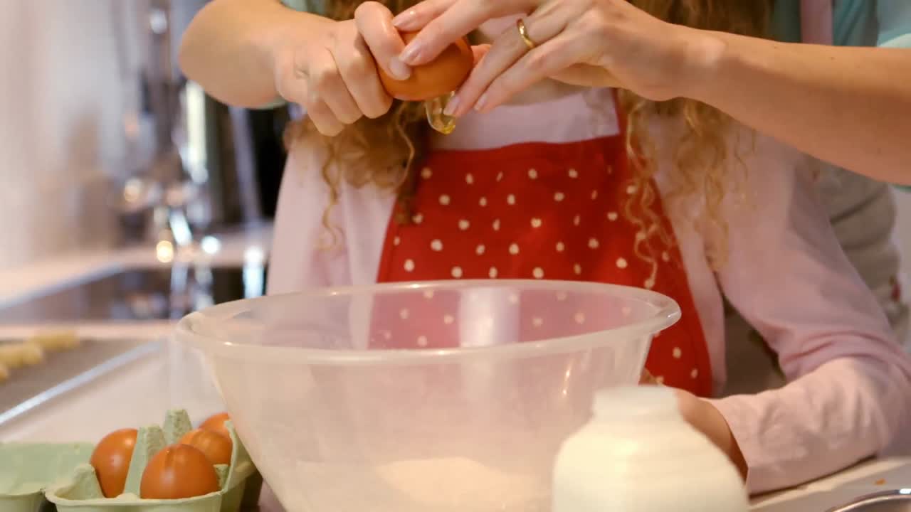 어머니 가 부 ⁇  에서 계란 을 부러뜨리는 딸 을 돕고 있다