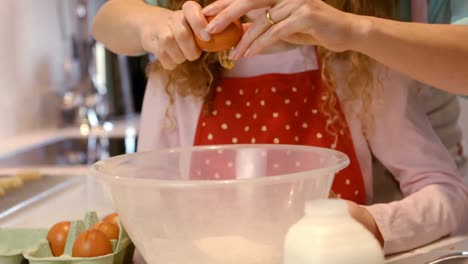 Mother-assisting-daughter-in-breaking-eggs-in-kitchen