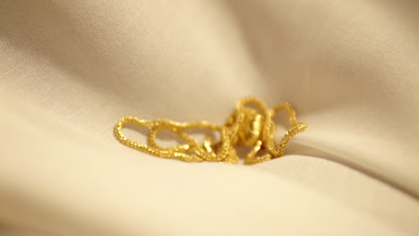 beautiful gold chain with heart pendant sliding over beige fabric in slow motion