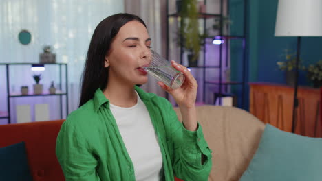 Thirsty-one-young-woman-sitting-at-home-holding-glass-of-natural-aqua-make-sips-drinking-still-water