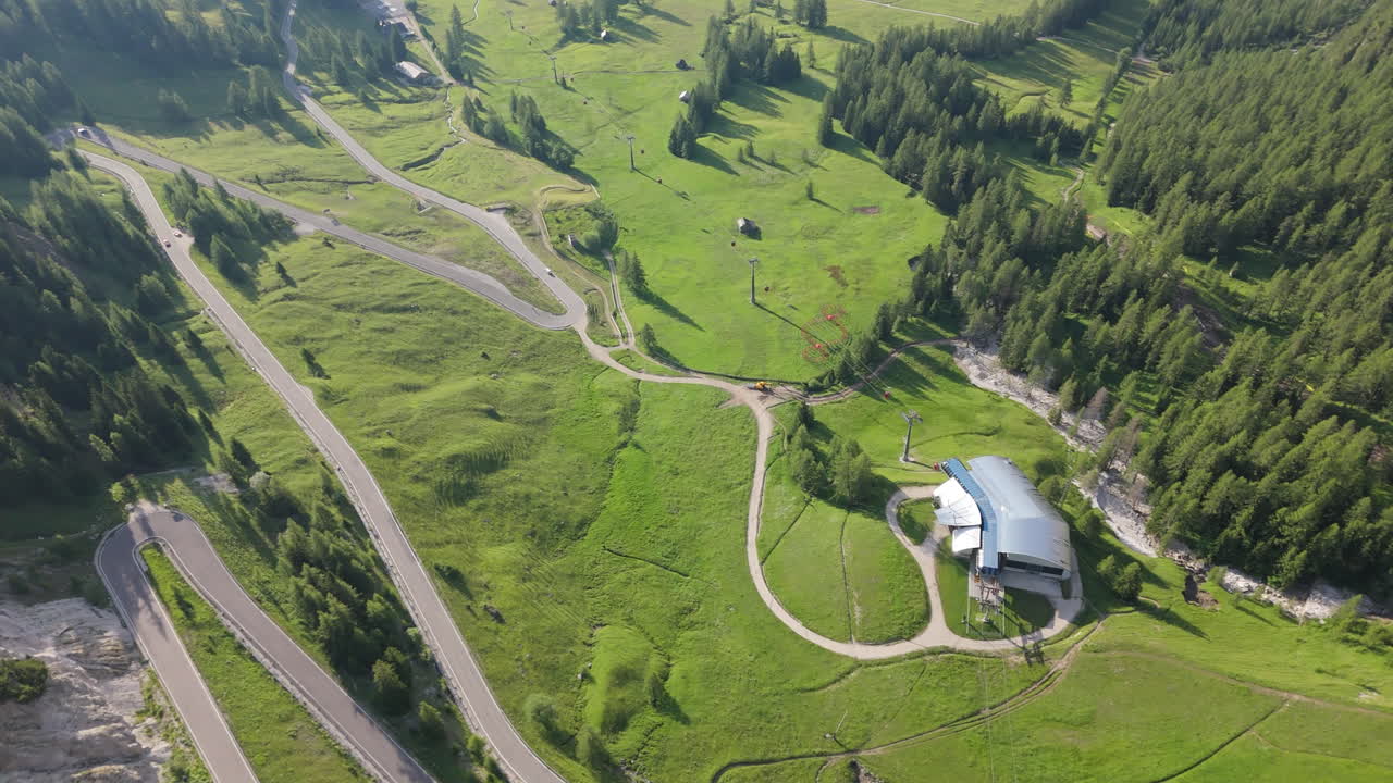 Drone footage of a ski lift station and winding alpine road in the Dolomites during summer, showing tourism and outdoor recreation