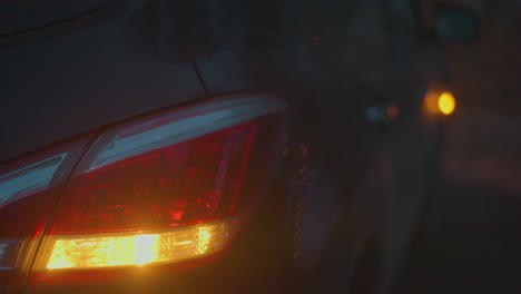 close-up of a car's tail light and turn signal illuminated in the dark, creating a blurred and moody atmosphere, the red and amber lights contrast against the dark background