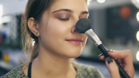 close up view of professional makeup artist's hands applying facial blusher on young woman's skin using special brush. slow motion