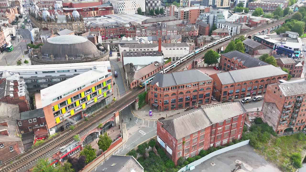 Aerial view of a modern passenger train traveling across a Victorian railway viaduct amid historic brick buildings in central Leeds, under bright daylight