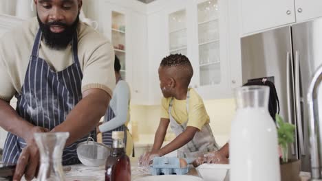 Happy-african-american-couple-with-son-and-daughter-in-aprons-preparing-meal-in-kitchen,-slow-motion