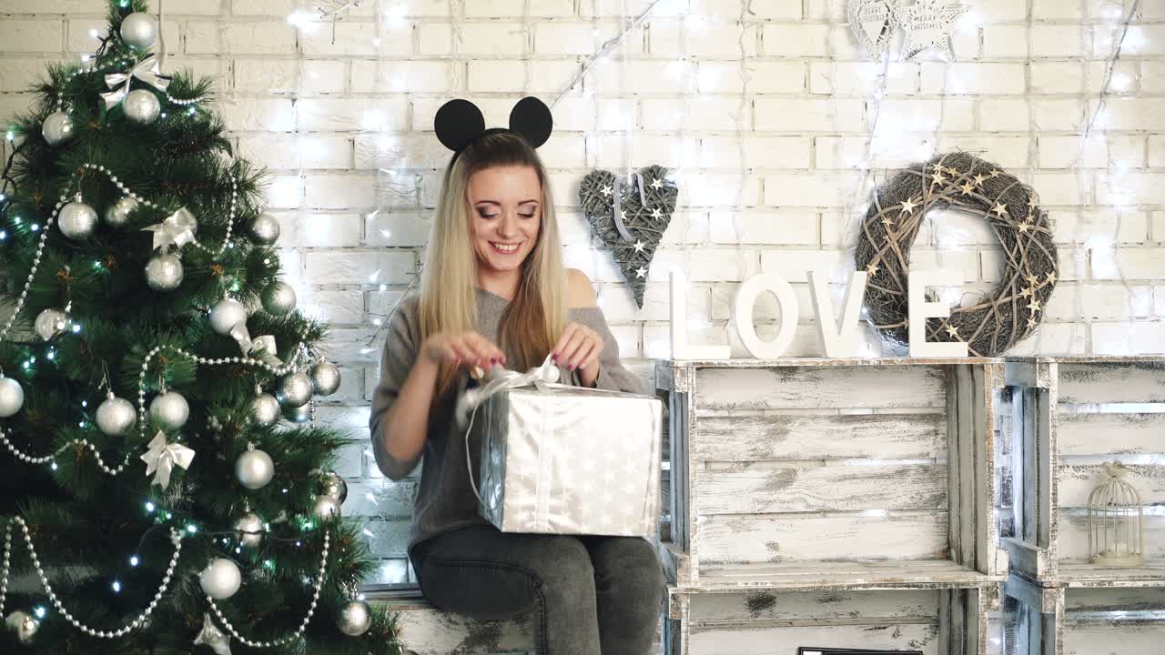 Woman celebration at Christmas atmosphere. Young woman posing with gift boxes in room decorated for Christmas