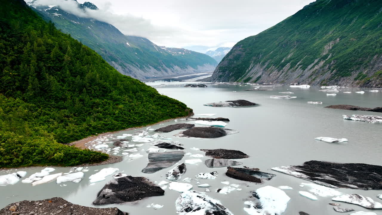 Footage above the river with boulders and pieces of ice. Approaching the mount covered with greenery. In the wilderness of Alaska, USA