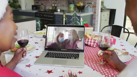 pareja afroamericana con vino usando computadora portátil para la videollamada de navidad con familia feliz en la pantalla
