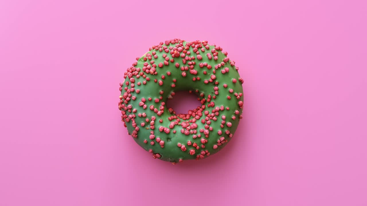 apetitoso rosquilla fresca brillante con glaseado verde girando aislado en rosa. cámara roja dragón 4k