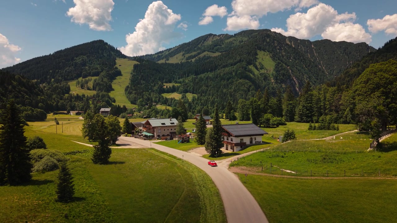 Auto d'epoca rossa cabriolet che guida lungo una strada di montagna oltre tradizionali chalet in legno nelle Alpi austriache. Vista aerea.