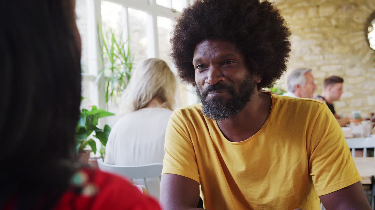 Middle aged black man eating breakfast and talking with his girlfriend at a restaurant, view over her shoulder, close up