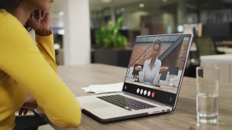 mujer biracial usando computadora portátil para videollamada, con un colega de negocios en la pantalla