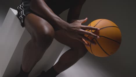 toma de estudio de cerca de un jugador de baloncesto masculino sentado con las manos sosteniendo la pelota 4