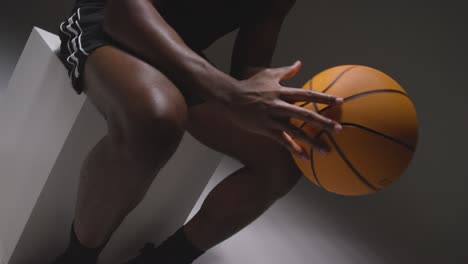 close up studio shot of seated male basketball player with hands holding ball 4