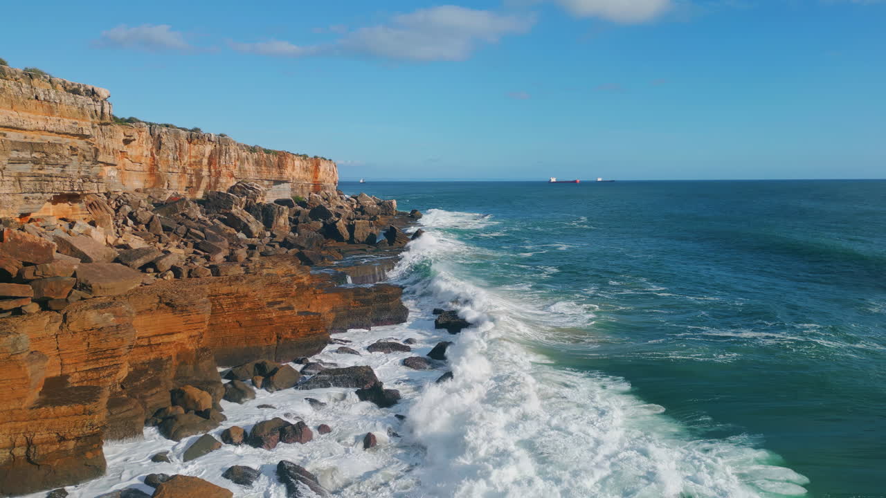 Drone sunny rocky seashore scenery with stormy foamy waves breaking coastline.