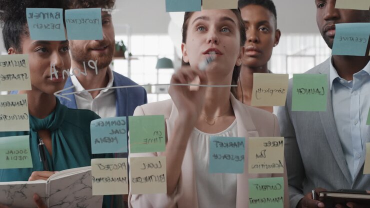 corporate business people using sticky notes brainstorming problem solving strategy on glass whiteboard team leader woman showing solution for project deadline in office meeting