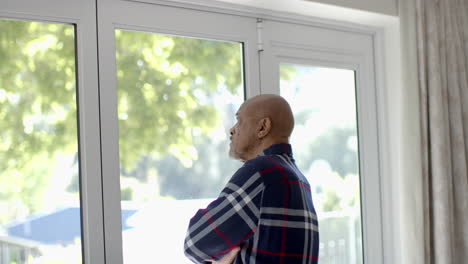 thoughtful senior biracial man looking through window at home, slow motion